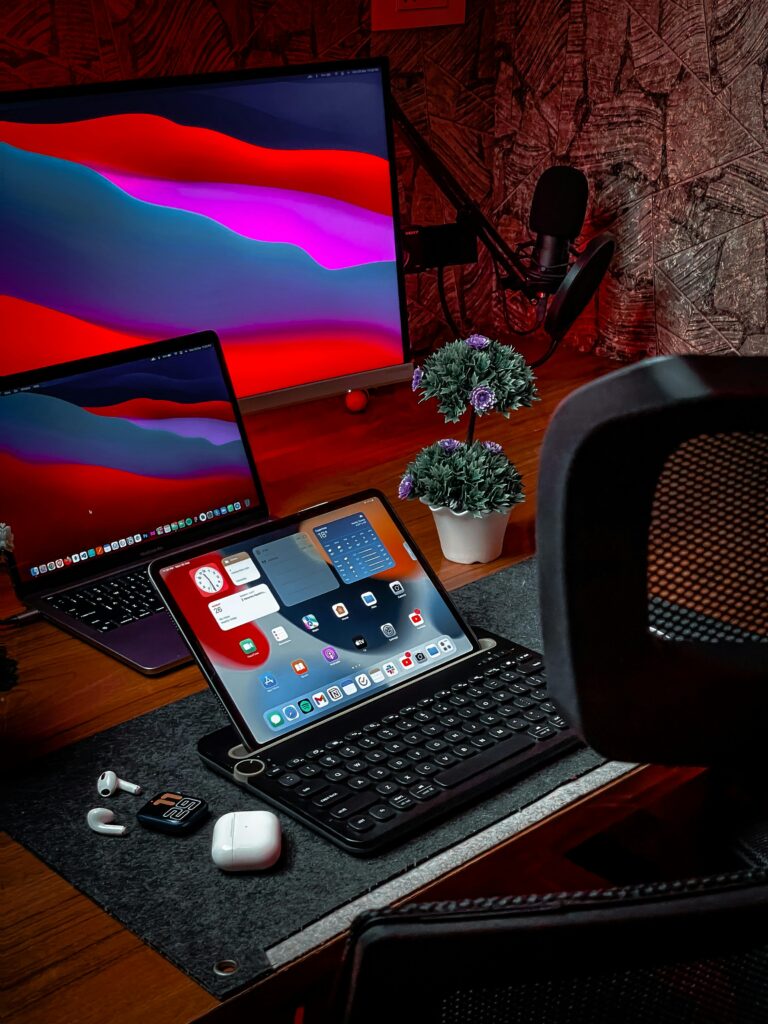 Cozy home office setup featuring iPad, MacBook, AirPods, and desktop with vibrant display.